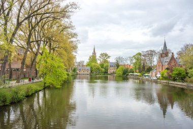 Aşk gölüne bakan yeşil yapraklı güzel ağaç, Belçika, Brugge 'deki Minnewater Gölü, bulutlu gökyüzü ile aydınlık bir yaz gününde