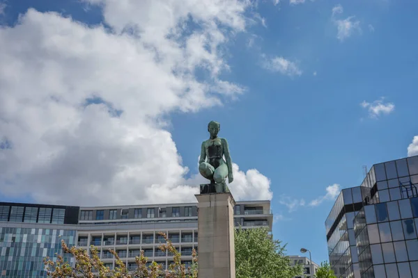 Sculpture of a man woman kneeling on the top of a pillar in Brussels, Belgium with a blue sky