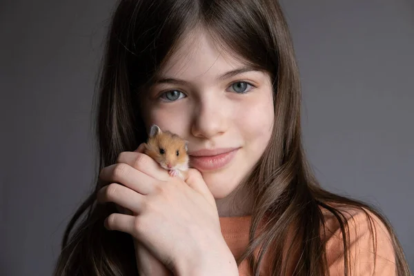 Küçük güzel kız, kollarında kızıl bir hamster tutuyor. Hayvanların ve çocukların arkadaşlığı, kavram