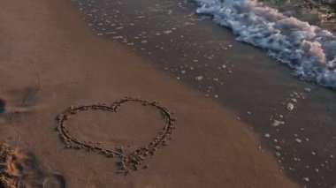 Deniz dalgası kuma çizilen kalbi temizler.