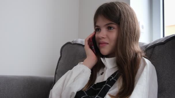 Liten, ung flicka sitter på soffan och pratar i telefon — Stockvideo
