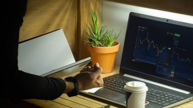 Evde çalışan genç ve mutlu bir işadamı dizüstü bilgisayar ve yazılar üzerinde borsa web sitesi kullanıyor- Genç Yatırım, ticaret ve iş tasarımı. Ev ofis konsepti. Yüz yok, sadece eller.