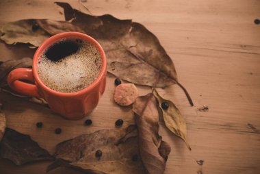 Sonbahar ya da sonbahar sabahı kahve konsepti. Turuncu kahve fincanı ve kırsal ahşap masa arkaplanı üzerine düşmüş sarı yapraklar, üst manzara, geniş kompozisyon. kopyalama alanı ile