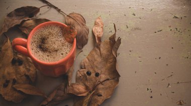 Sonbahar ya da sonbahar sabahı kahve konsepti. Turuncu kahve fincanı ve gri kırsal ahşap masa arkaplanı üzerine düşmüş sarı yapraklar, üst manzara, geniş kompozisyon. kopyalama alanı ile