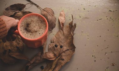 Erkek eli sıcak kahve kapuçino, turuncu süveter ve eski gri ahşap arka planda sonbahar yaprakları tutuyor. Antika tonlar. Sonbahar rahatlama konsepti. Boşluğu kopyala