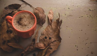 Sonbahar ya da sonbahar sabahı kahve konsepti. Turuncu kahve fincanı ve gri kırsal ahşap masa arkaplanı üzerine düşmüş sarı yapraklar, üst manzara, geniş kompozisyon. kopyalama alanı ile