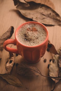 Sonbahar ya da sonbahar sabahı kahve kavramı dikey. Turuncu kahve fincanı ve kırsal ahşap masa arkaplanı üzerine düşmüş sarı yapraklar, üst manzara, geniş kompozisyon. kopyalama alanı ile