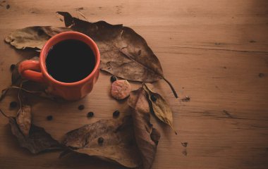 Sonbahar ya da sonbahar sabahı kahve konsepti. Bir kupa kahve ve ahşap masa arkaplanının üzerine düşmüş sarı yapraklar, üst manzara, geniş kompozisyon. kopyalama alanı ile