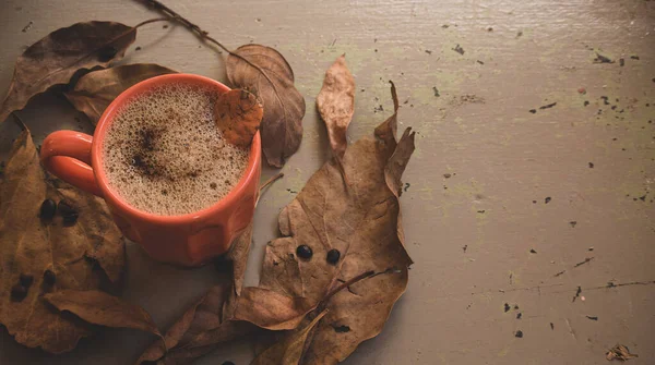 Sonbahar ya da sonbahar sabahı kahve konsepti. Turuncu kahve fincanı ve gri kırsal ahşap masa arkaplanı üzerine düşmüş sarı yapraklar, üst manzara, geniş kompozisyon. kopyalama alanı ile