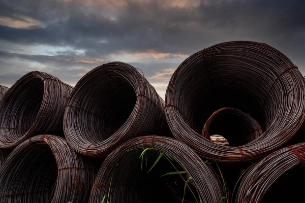 Steel wire coil against dark sky. Metal steel reinforced for concrete construction. Iron wire for construction industry. Spool or roll of silver steel wire. Metal materials. Rusty steel wire coil.