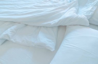 Modern yatak odasında beyaz rahat yatak ve yumuşak yastık. Otel odasında beyaz çarşaf battaniyesi. Sabah uyandıktan sonra dağınık beyaz battaniyenin yakın çekim ayrıntıları. Yumuşak beyaz yorganı olan rahat bir yatak.. 