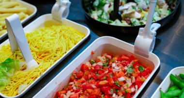 Restoranda salata büfesi. Öğle veya akşam yemeği için taze salata büfesi. Sağlıklı yiyecekler. Tezgahtaki beyaz kasede doğranmış domates ve sarı erişte. Yemek servisi. Ziyafet servisi. Vejetaryen yemeği..