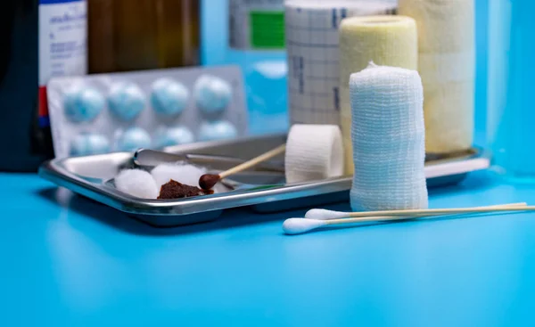 Wound care dressing set. Selective focus cotton stick and elastic conforming bandage, stainless steel plate on blur forceps, bandage, cotton ball with alcohol. Medical supply on blue background.