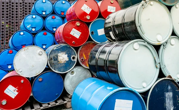 Old chemical barrels on wooden pallet. Blue and red oil drum. Steel and plastic oil tank. Toxic waste warehouse. Hazard chemical barrel. Industrial waste in drum. Hazard waste storage in factory.