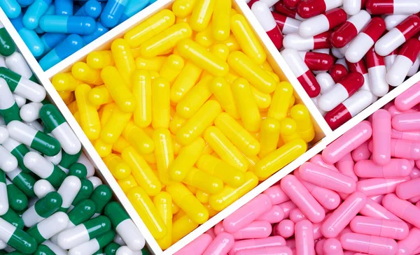 Top view colorful capsule pills in a plastic tray. Yellow, pink, red, green, and blue capsule pills. Antibiotics, vitamins, and supplements capsules. Pharmaceutical industry. Prescription drugs.