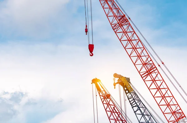 Crawler crane against blue sky and white clouds. Real estate industry. Red crawler crane use reel lift up equipment in construction site. Crane for rent. Crane dealership for construction business.