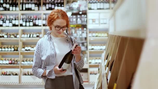 Mujer Pelirroja Atractiva Cuidadosamente Elegir Botella Vino Tienda Comestibles Moderna — Vídeos de Stock