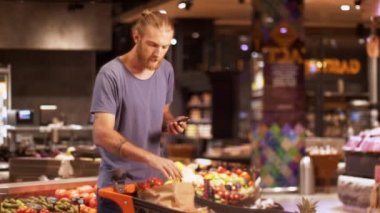 Arabası mal dolu yakışıklı adam modern süpermarkette akıllı telefondan ürün listesini dikkatle kontrol ediyor. Sıradan bir adam, marketten her şeyin alınıp alınmadığını kontrol ediyor.