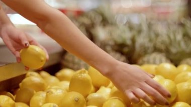 Kadın satıcıyı kapatın ve markette taze limon düzenleyin. Kadın elleri modern marketten taze limon seçiyor.