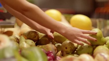 Markette meyve seçen yakın bir kadın. Genç satıcı bir süpermarkette meyve ve sebze reyonuna taze armut seriyor.