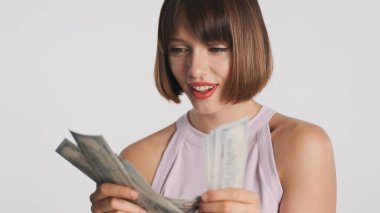 Çekici, gülümseyen, kısa saçlı, para sayan esmer kız beyaz arka planda heyecanlı görünüyor.