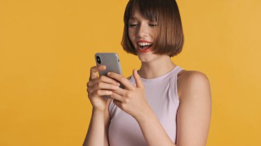 Oldukça neşeli esmer kız sarı arka planda izole edilmiş sosyal ağdaki arkadaşlarıyla çevrimiçi sohbetten hoşlanıyor. Mutlu ifade