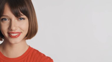 Kısa saçlı ve kırmızı dudaklı güzel esmer kızı kapayın. Beyaz arka planda reklam ya da tanıtım metni için kameraya bakarken mutlu olun.