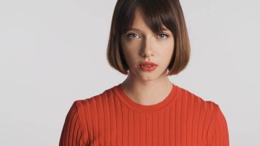 Çekici esmer kızın portresi kısa saçlı ve kırmızı dudaklı beyaz arka planda izole edilmiş kameraya şehvetle bakıyor.