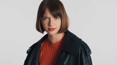 Gündelik giyinmiş şaşkın esmer kız beyaz arka planda izole edilmiş kameraya dikkatlice bakıyor.