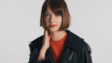 Gündelik giyinmiş kafası karışmış esmer kız beyaz arka planda izole edilmiş kamerada şaşkın görünüyor.