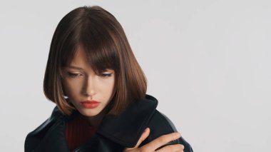 Üzgün, utangaç, esmer, kısa saçlı, beyaz arka planda izole bir şekilde kameraya poz veren kız. Üzücü ifade 