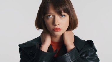 Kamerada poz veren üzgün esmer kız beyaz arka planda afallamış görünüyor. Yüz ifadesi 