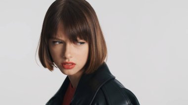 Kızgın esmer kız, kısa saçlı ve kırmızı dudaklı. Huysuz bir ifadeyle beyaz arka planda izole edilmiş.