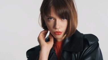 Kısa saçlı, kırmızı dudaklı, beyaz arka planda ciddi görünen esmer bir moda kızı. Profesyonel model stüdyoda poz veriyor.