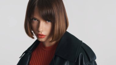 Kısa saçlı, kırmızı dudaklı, kameraya şeytan gibi poz veren güzel bir moda kızı beyaz arka plana bakıyor. Ciddi kız.