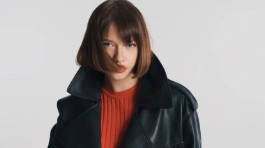 Kısa saçlı, kırmızı dudaklı, kameraya poz veren genç manken beyaz arka plandan kameraya bakıyor.