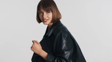 Çekici pozitif esmer kız gündelik giyinmiş mutlu bir şekilde kameraya bakıyor ve beyaz arka planda izole bir şekilde gülümsüyor.