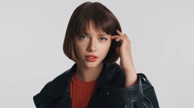 Kısa saçlı, kırmızı dudaklı güzel esmer kız beyaz arka planda dalgın dalgın duruyor. Stüdyoda kameraya bakan düşünceli kız.