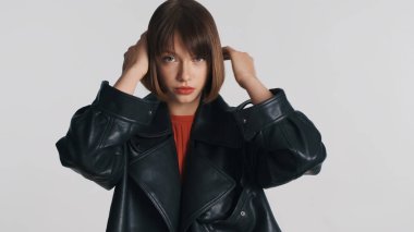 Çekici stil sahibi esmer kız saç kesimini güzelleştiriyor beyaz arka plandan kameraya bakıyor.