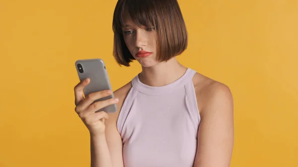Upset brunette girl with bob hair looking sad get message from boyfriend on smartphone over colorful background