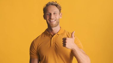 Çekici sarışın, sakallı bir adam mavi arka planda baş parmağını gösteriyor ve gülümsüyor. Jest gibi