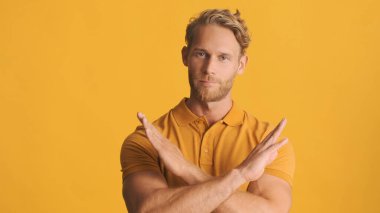 Yakışıklı, sarışın, sakallı bir adam. Renkli bir arkaplanda el ele tutuşarak kamera karşısına geçmiş. İfade yok