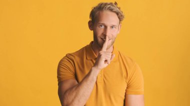 Çekici, sarışın, sakallı adam renkli arka planda sessiz bir jest yapıyor. Gizli ifadeyi koru 