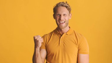 Sarışın, çekici ve sakallı bir adam, sarı arka planda izole edilmiş kameraya 