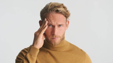 Genç, sarışın, sakallı adam beyaz arka planda şakaklarda acı gösteriyor.