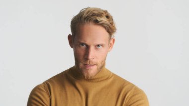 Genç agresif sarışın sakallı adam beyaz arka planda izole edilmiş kameraya kızgın bakıyor. Ciddi ifade