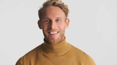 Sıradan giyinmiş yakışıklı sarışın adam beyaz arka planda izole edilmiş kamerada gülümsüyor.