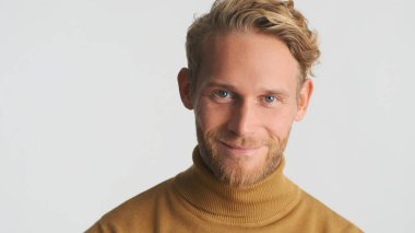 Sarışın sakallı adamın portresi mutlu bir şekilde kameraya bakıyor ve beyaz arka planda izole bir şekilde gülümsüyor. Stüdyoda çekici erkek model