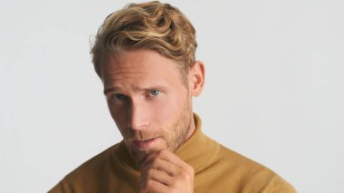 Yakışıklı, sarışın, sakallı adam beyaz arka planda izole edilmiş kamerada kendine güveniyor. Stüdyoda poz veren erkek model.