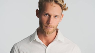 Gömlekli, sarışın ve sakallı genç iş adamı beyaz arka planda izole edilmiş kameraya bakıyor.